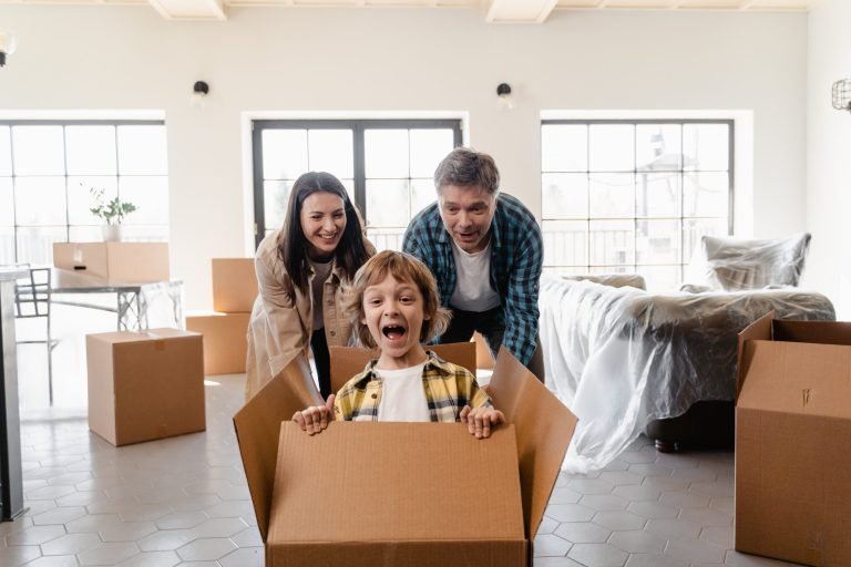 Happy family enjoying moving day with Crazy Removals, kid playing in a box amidst packing.